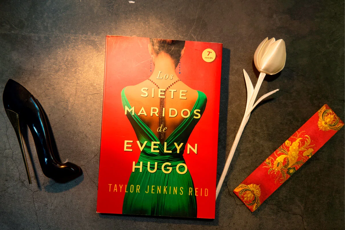 Los siete maridos de Evelyn Hugo de Taylor Jenkins Reid junto a un tacón negro, un tulipán blanco y un marcapáginas rojo