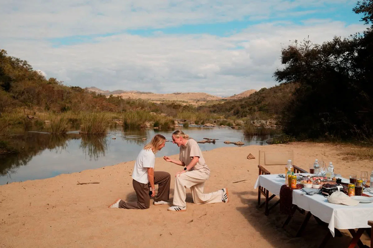 Millie Turner y Lisa Naalsund, jugadoras del Manchester United, arrodilladas en la arena junto a un río durante su pedida de compromiso en un safari en el Kruger National Park